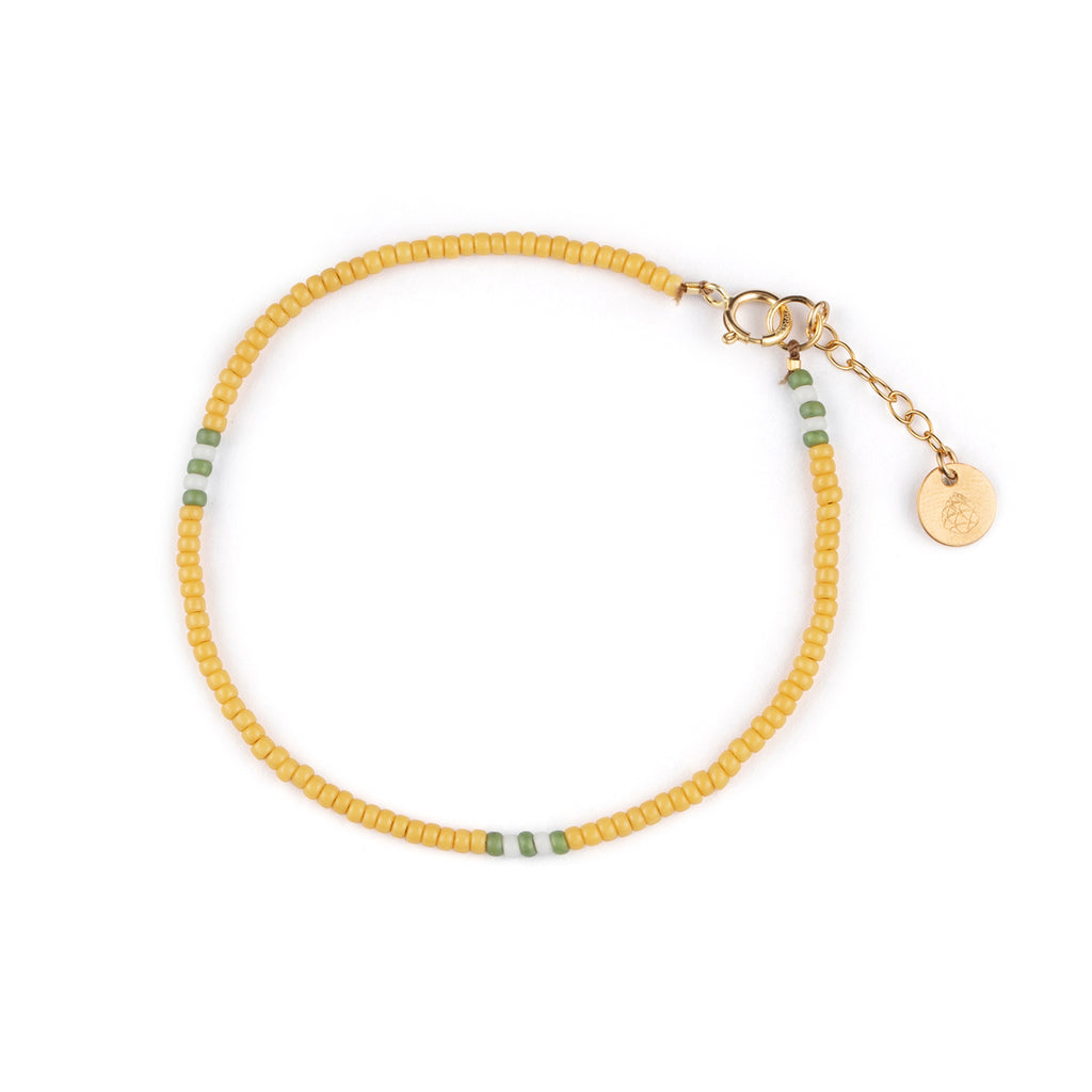 A beaded bracelet features small yellow beads, interspersed with green and white beads. Adjustable in size with a 14k gold fill adjuster chain.